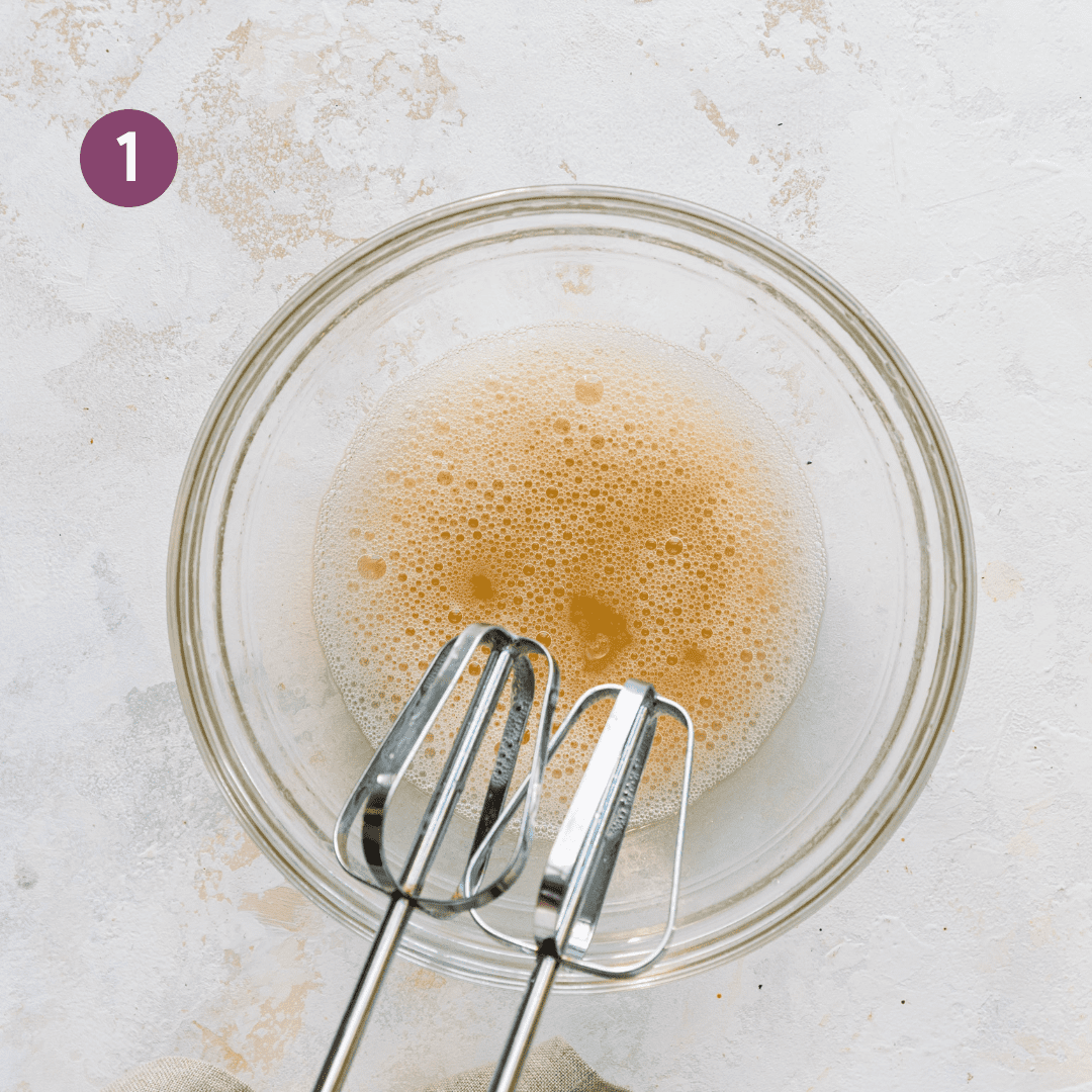 electric mixer whipping aquafaba in a glass bowl.