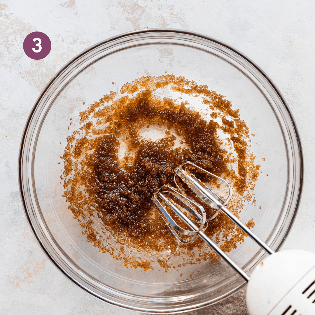 electric mixer whipping brown sugar and oil in a glass bowl.