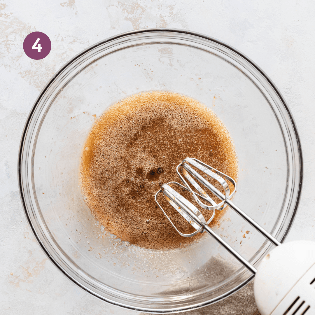 electric mixer whipping brown sugar and oil in a glass bowl.