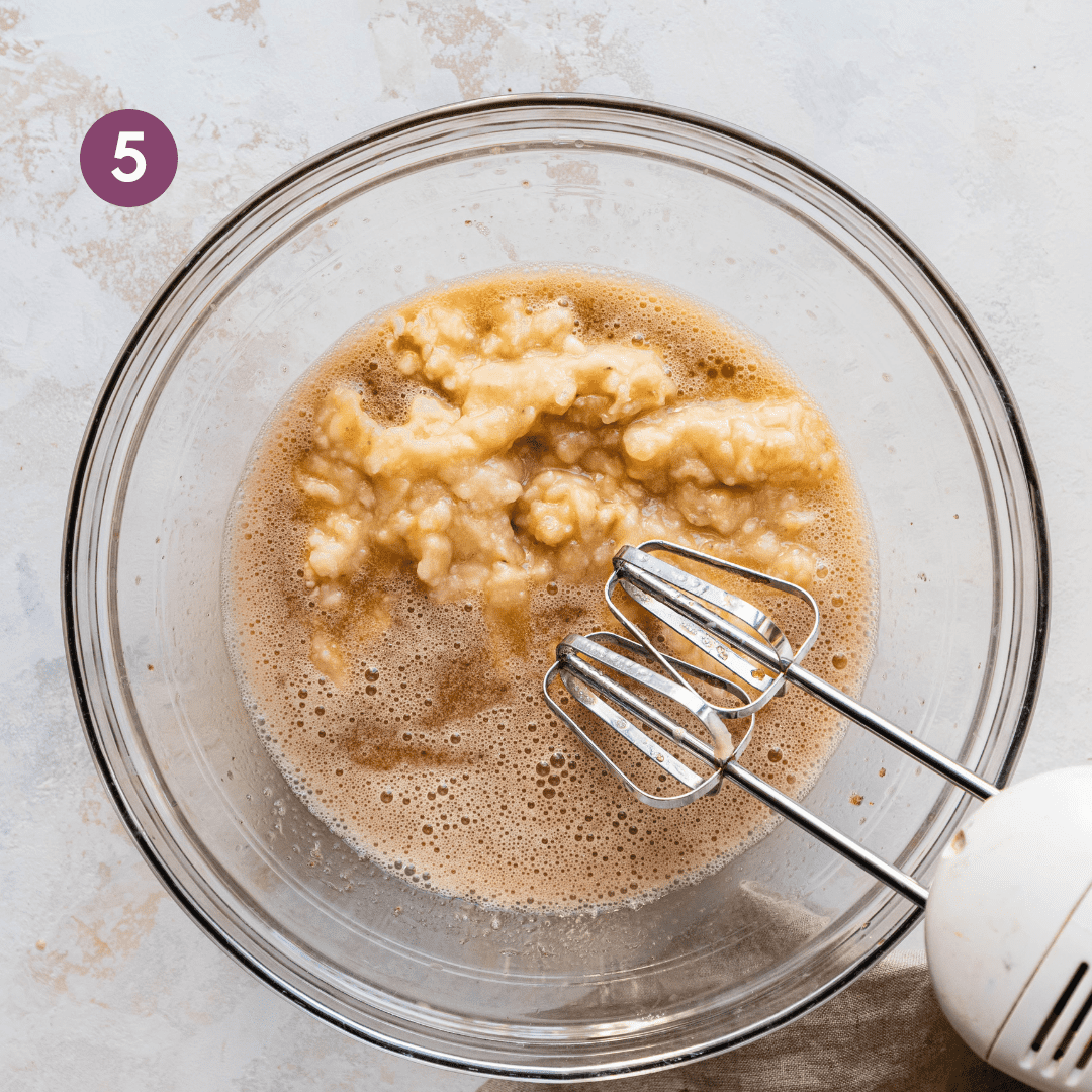 electric mixer whipping mashed bananas, brown sugar and oil in a glass bowl.