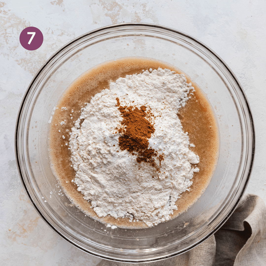 flour, salt, and spices sitting on top of liquid ingredients for vegan banana bread in a glass bowl.