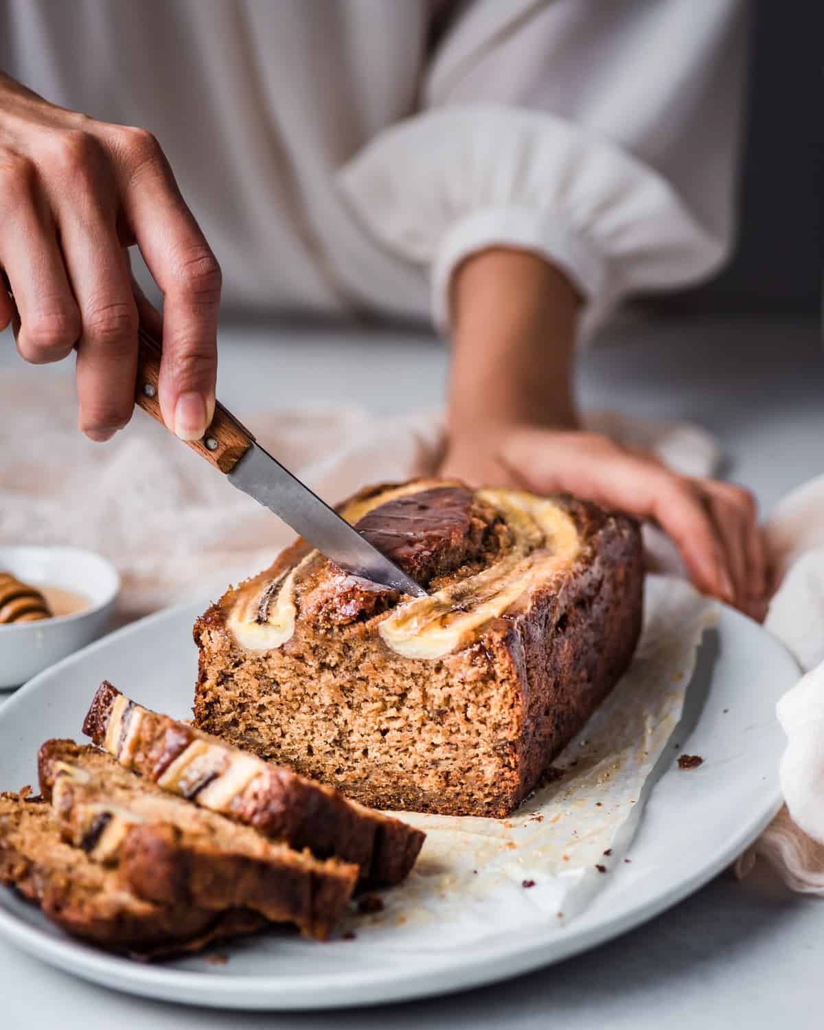 woman's hands slicing into a beautiful vegan banana bread on a platter.