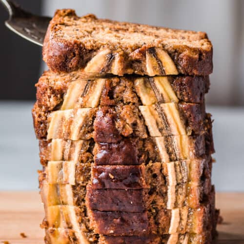 cake server lifting a slice of vegan banana bread from a tall stack of beautiful slices.