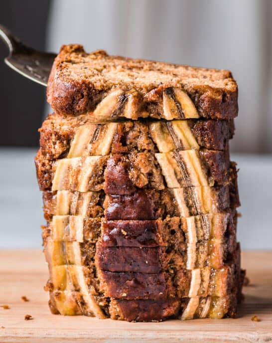 cake server lifting a slice of vegan banana bread from a tall stack of beautiful slices.