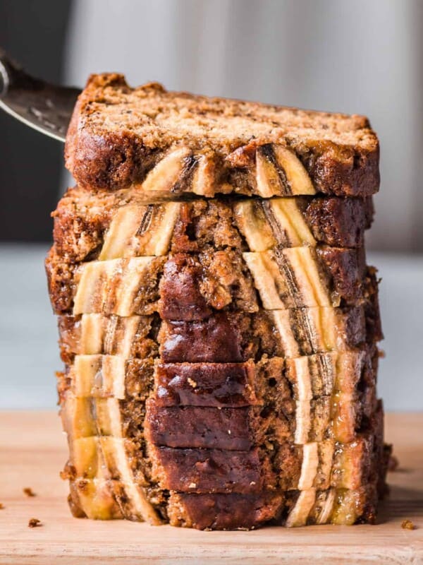 cake server lifting a slice of vegan banana bread from a tall stack of beautiful slices.