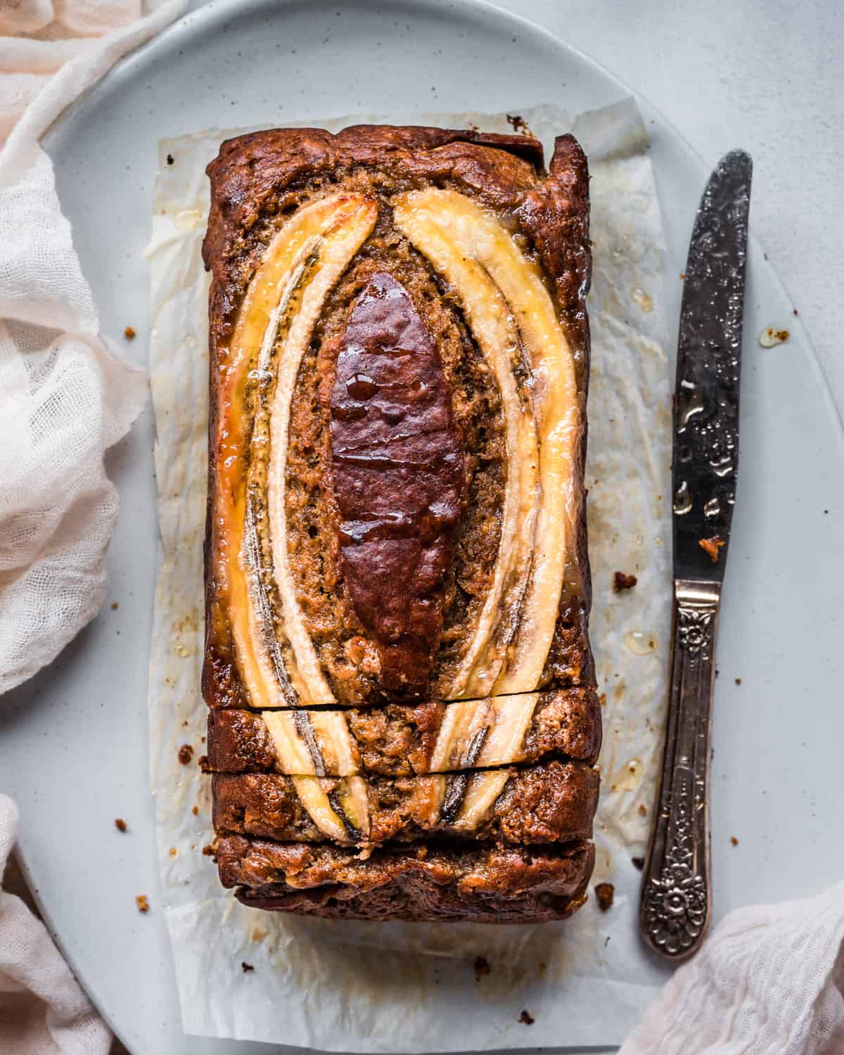 overhead shot of a beautiful vegan banana bread with a banana slice baked into the top, drizzled with honey, on a platter.