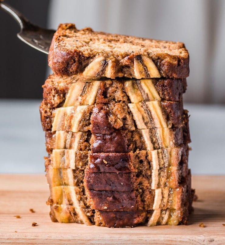 side view of sliced banana bread sitting upright with woman grabbing one with a pie server