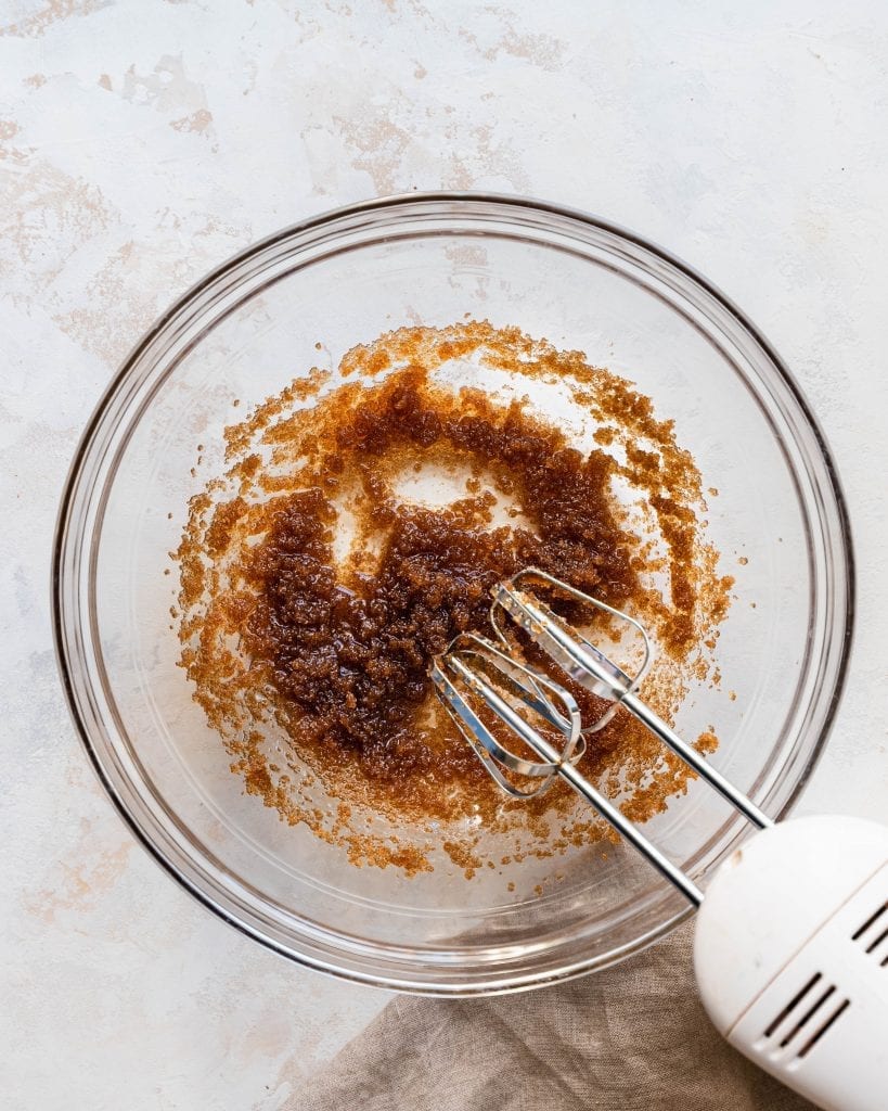 brown sugar and oil being mixed together in a bowl by an electric mixer
