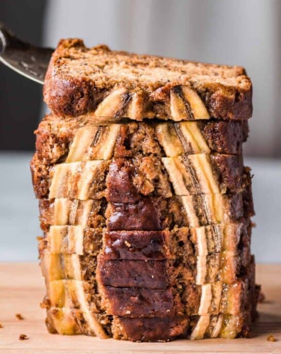 cake server lifting a slice of vegan banana bread from a tall stack of beautiful slices.