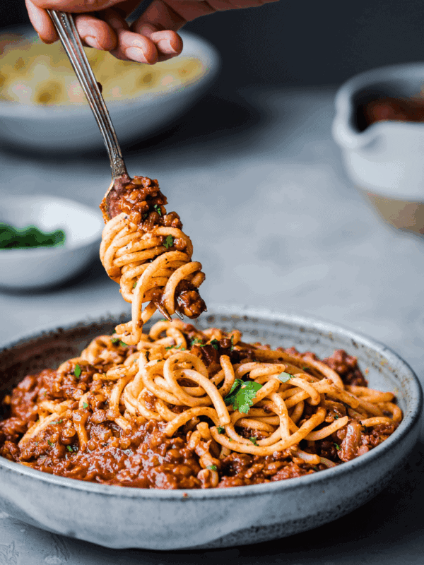 a fork twirling spaghetti in a bowl of red lentil bolognese.