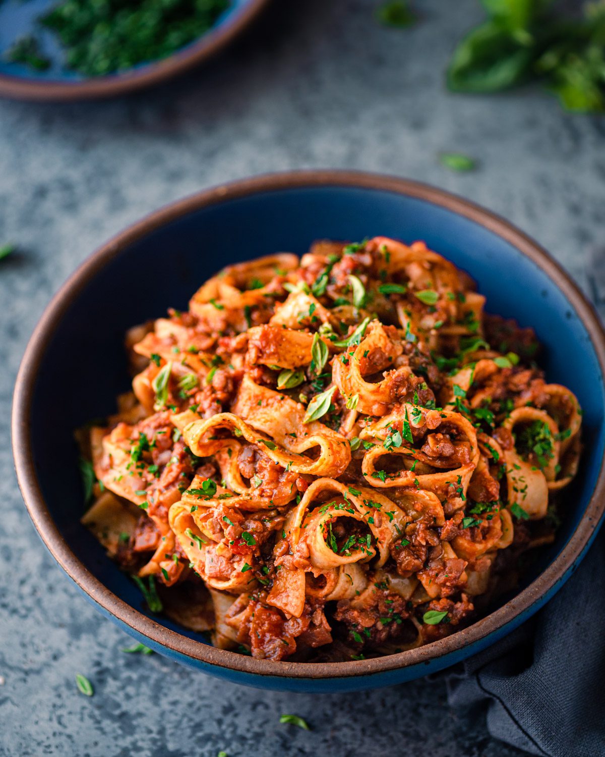 vegan lentil bolognese with wide pasta noodles in a blue bowl on a blue table.