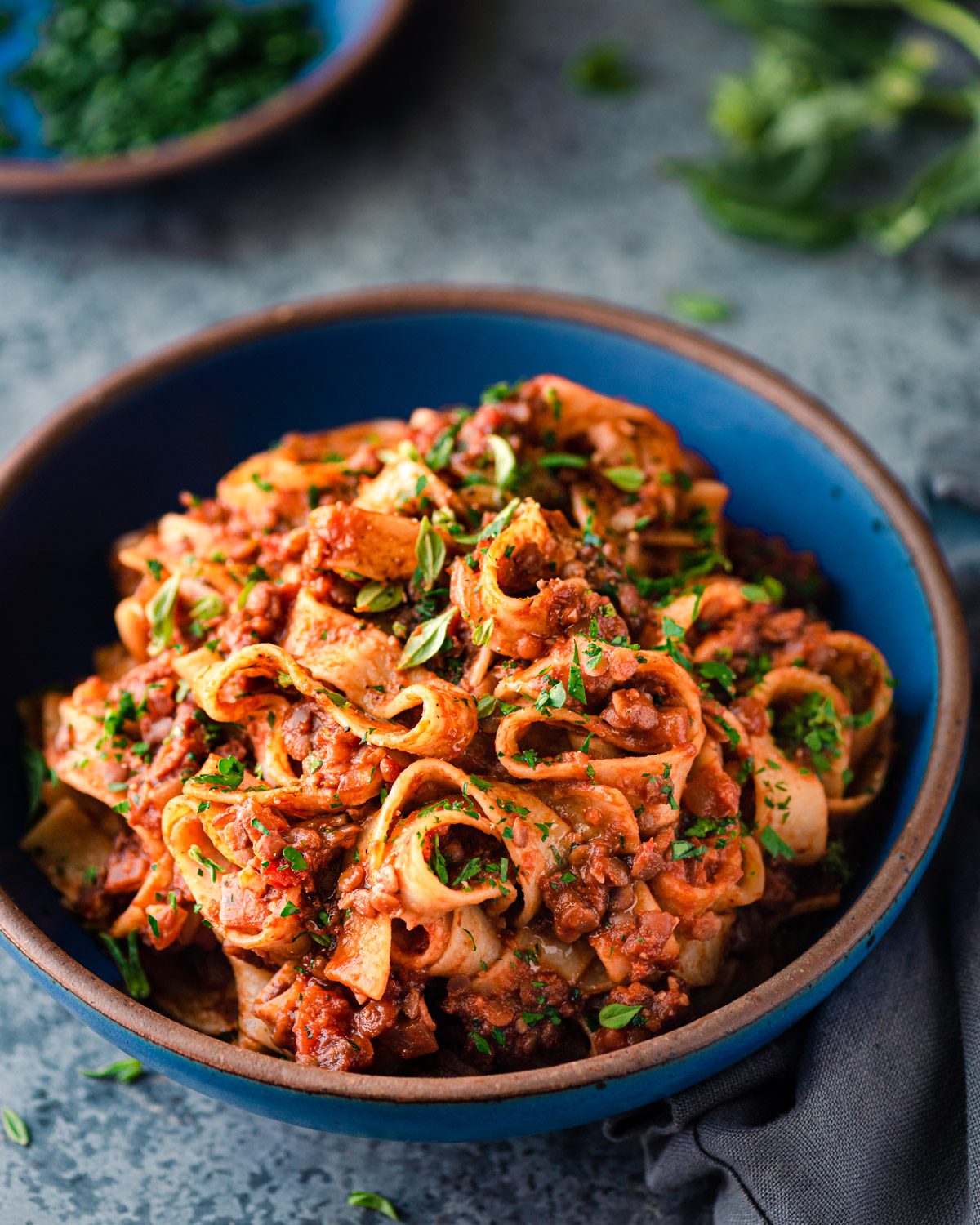 lentil bolognese with wide pasta noodles in a blue bowl on a blue table.