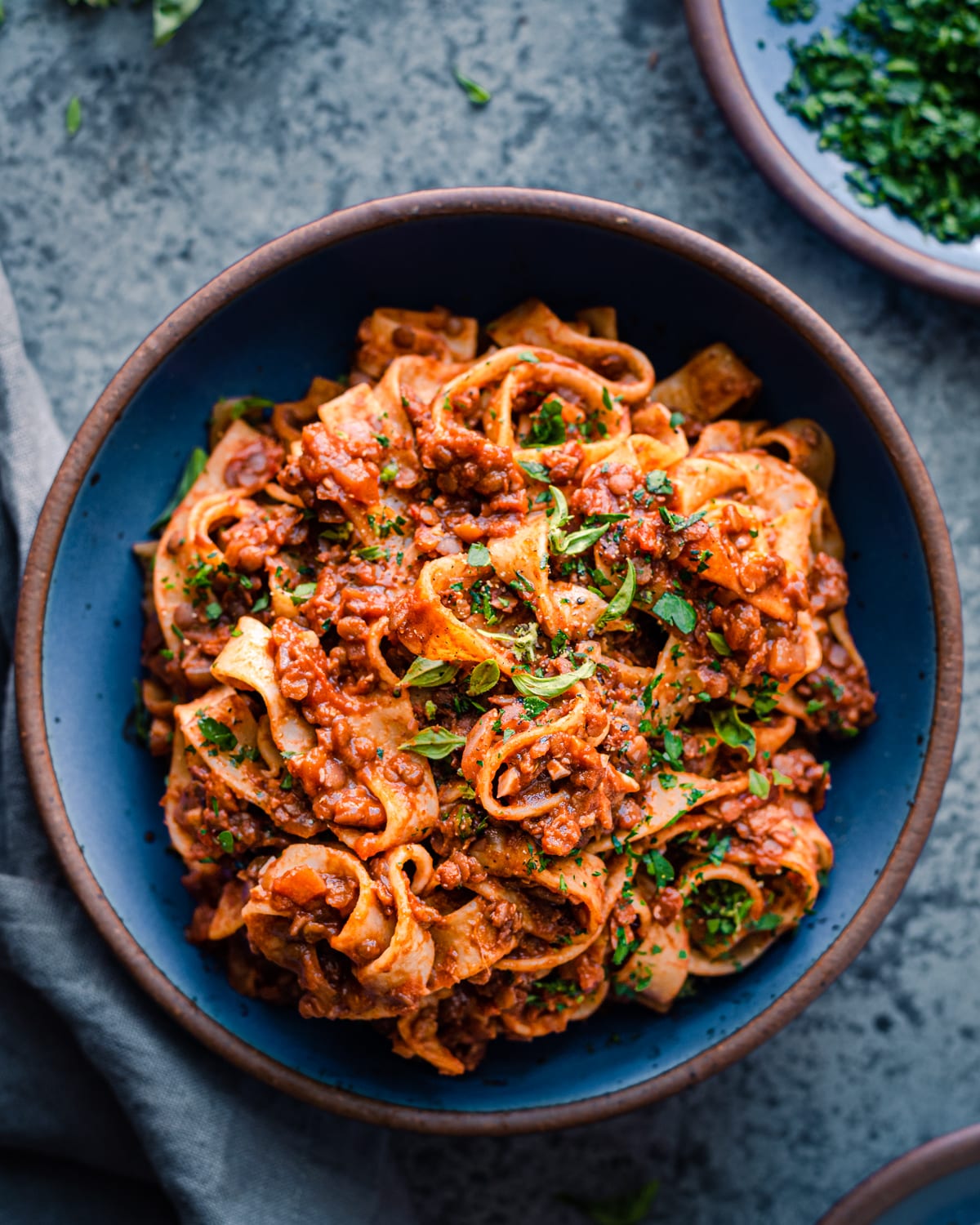 vegan lentil bolognese with wide pasta noodles in a blue bowl on a blue table.