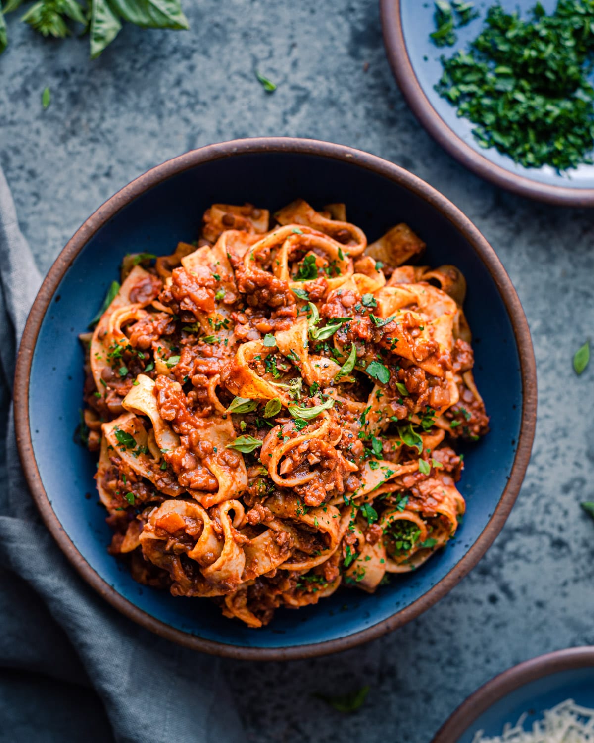 vegan lentil bolognese with wide pasta noodles in a blue bowl on a blue table.