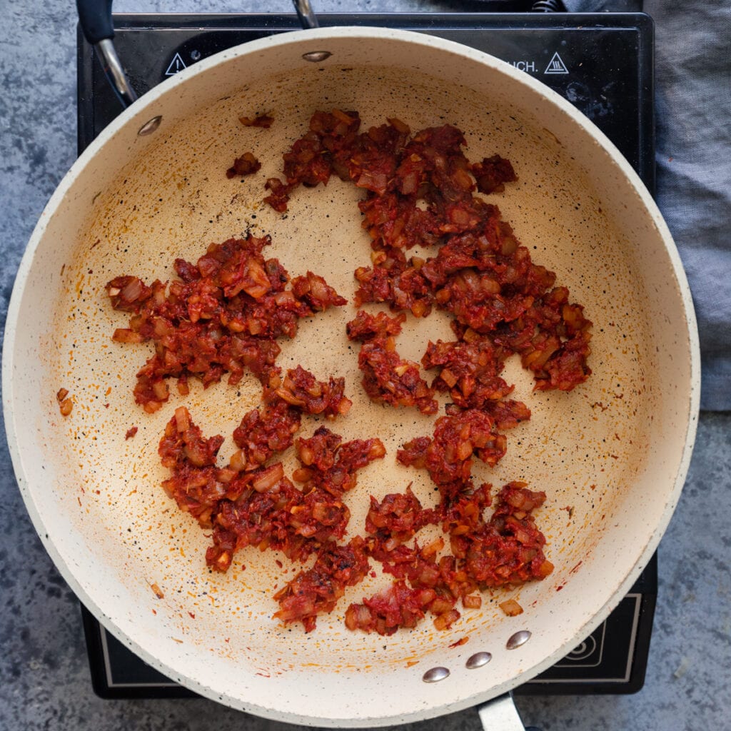 tomato paste mixed into onions in a saute pan