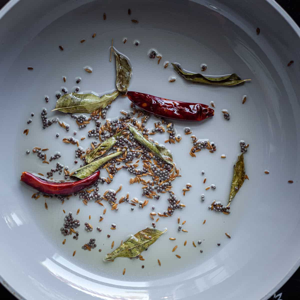 mustard seeds, cumin seeds, curry leaves, and chili peppers in oil for tadka