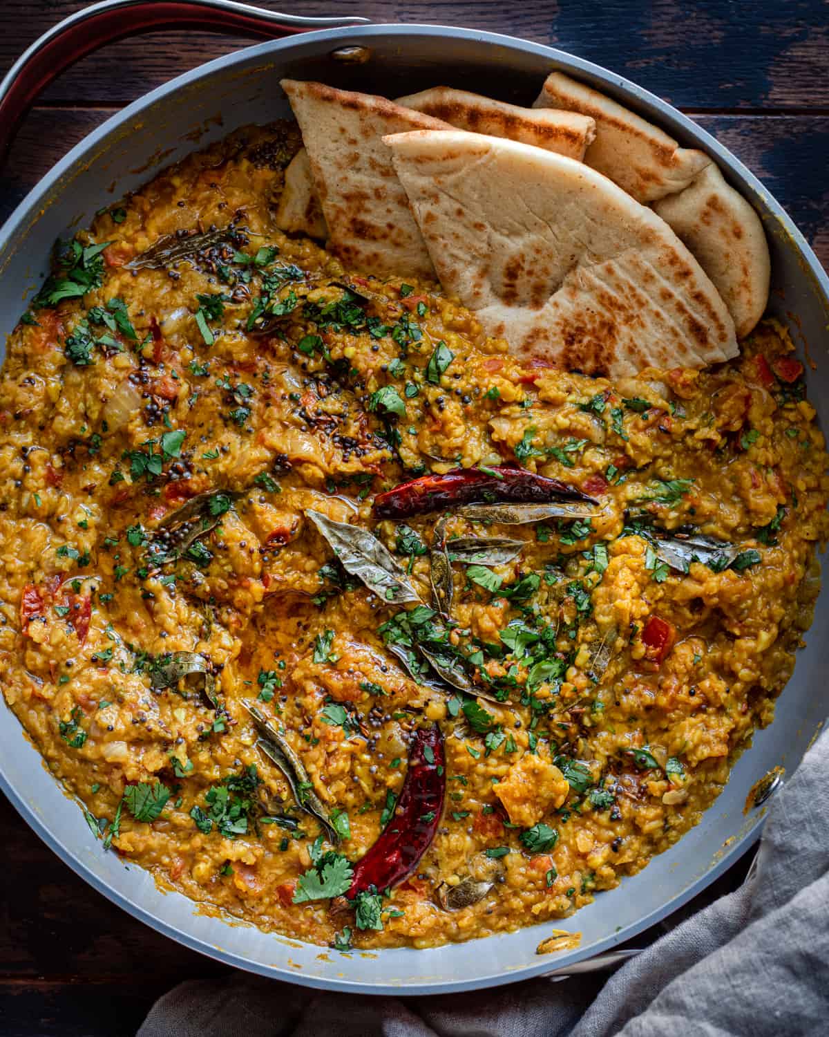 dal tadka in a frying pan, garnished with tadka and cilantro, with naan on the side