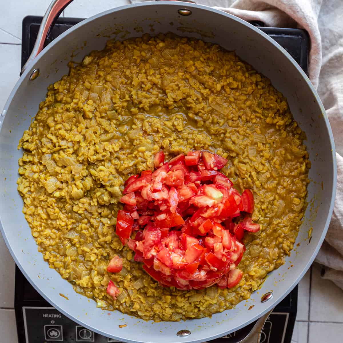 diced tomatoes on top of cooked dal in frying pan