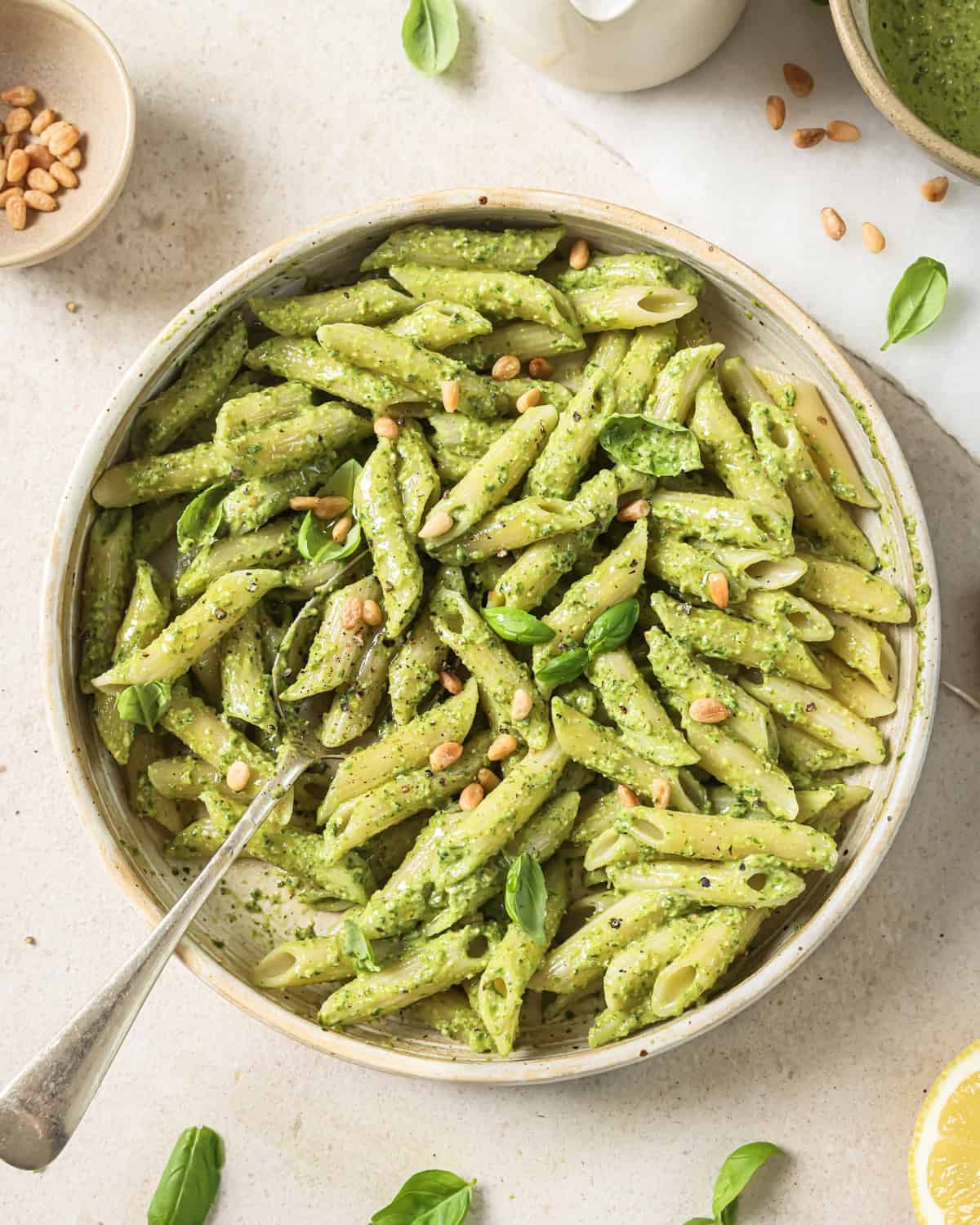 white bowl of penne pasta with pesto tossed in.