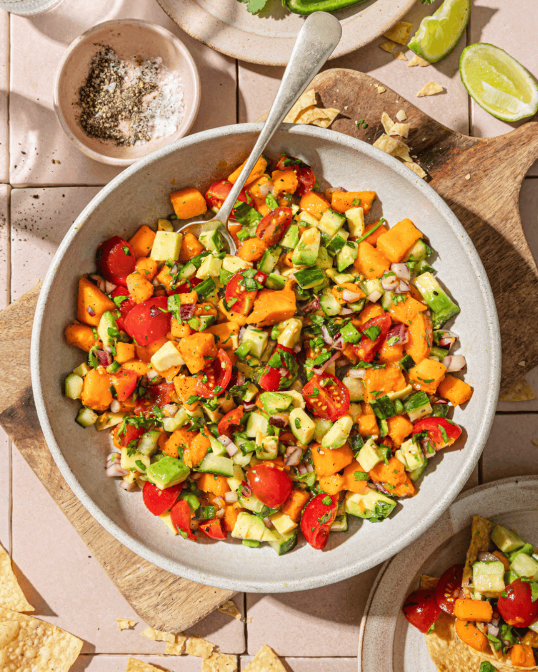 large bowl of mango avocado salsa surrounded by ingredient bowls and chips on the table.