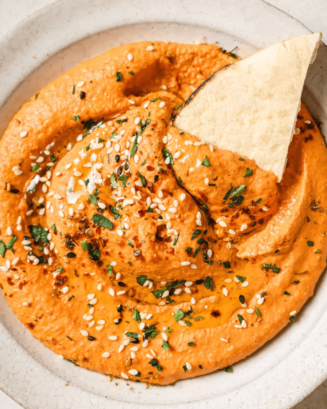 roasted red pepper hummus and a piece of pita in a bowl.