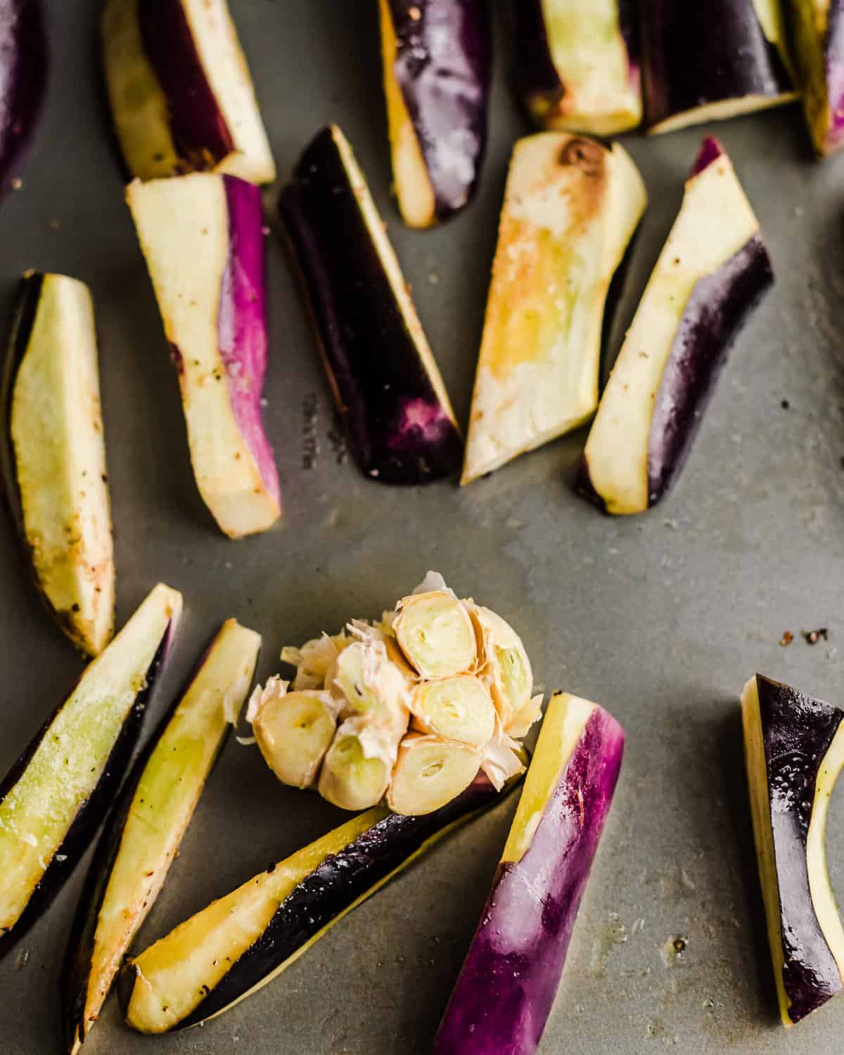 whole head of garlic on a sheet pan with eggplant wedges.