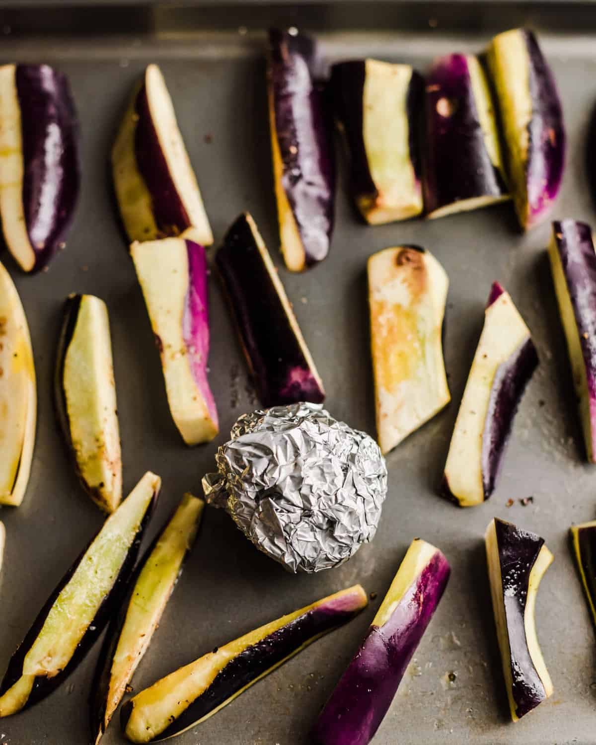 whole head of garlic wrapped in foil on a sheet pan with eggplant wedges.