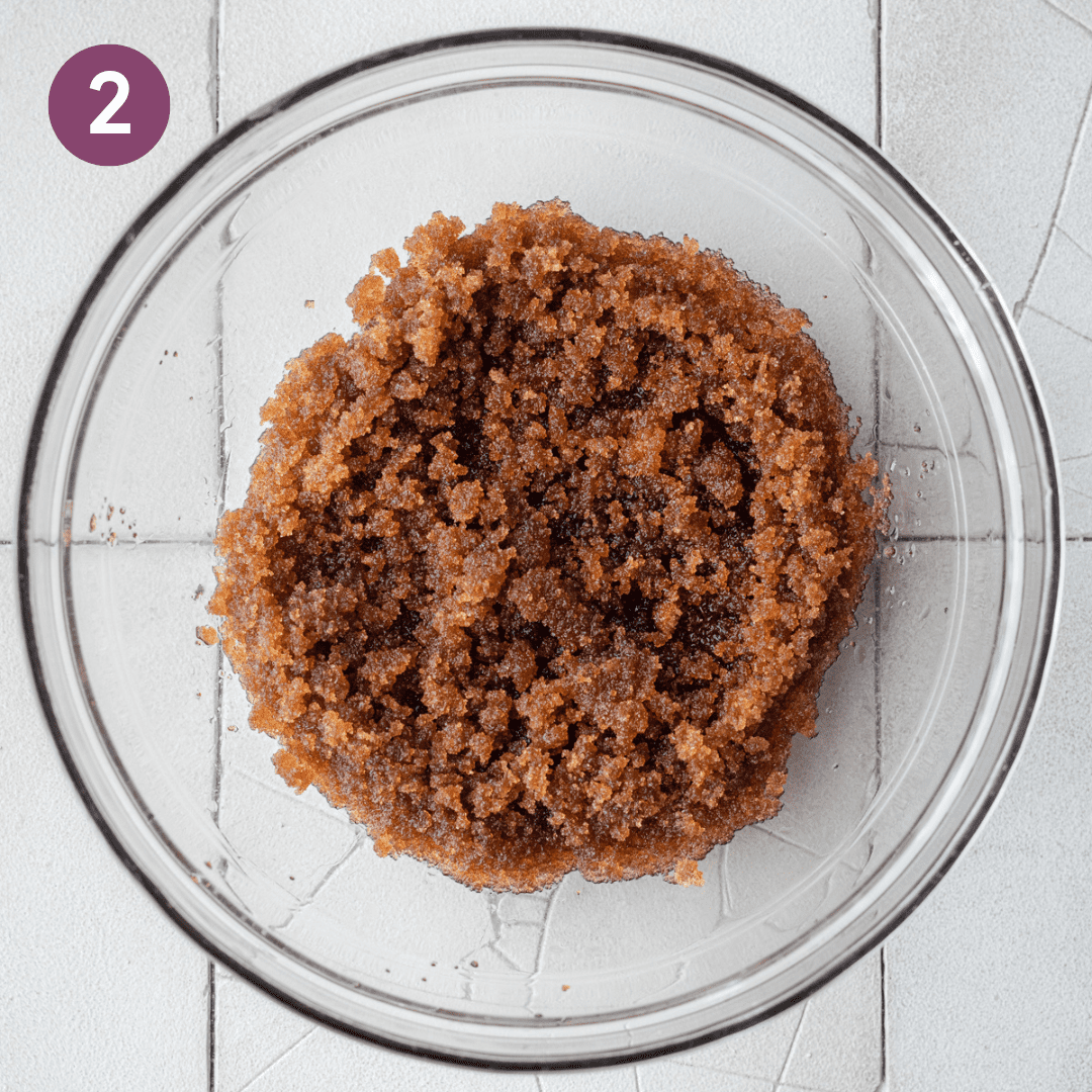 brown sugar and oil mixed together in a glass bowl on a white tiled surface.