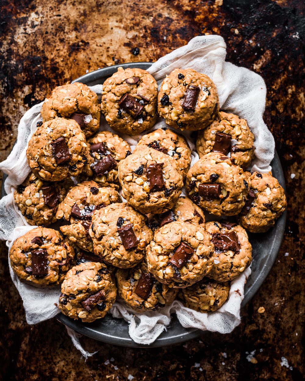 Plate of chocolate chunk cookies on a cloth napkin on a metal tin.