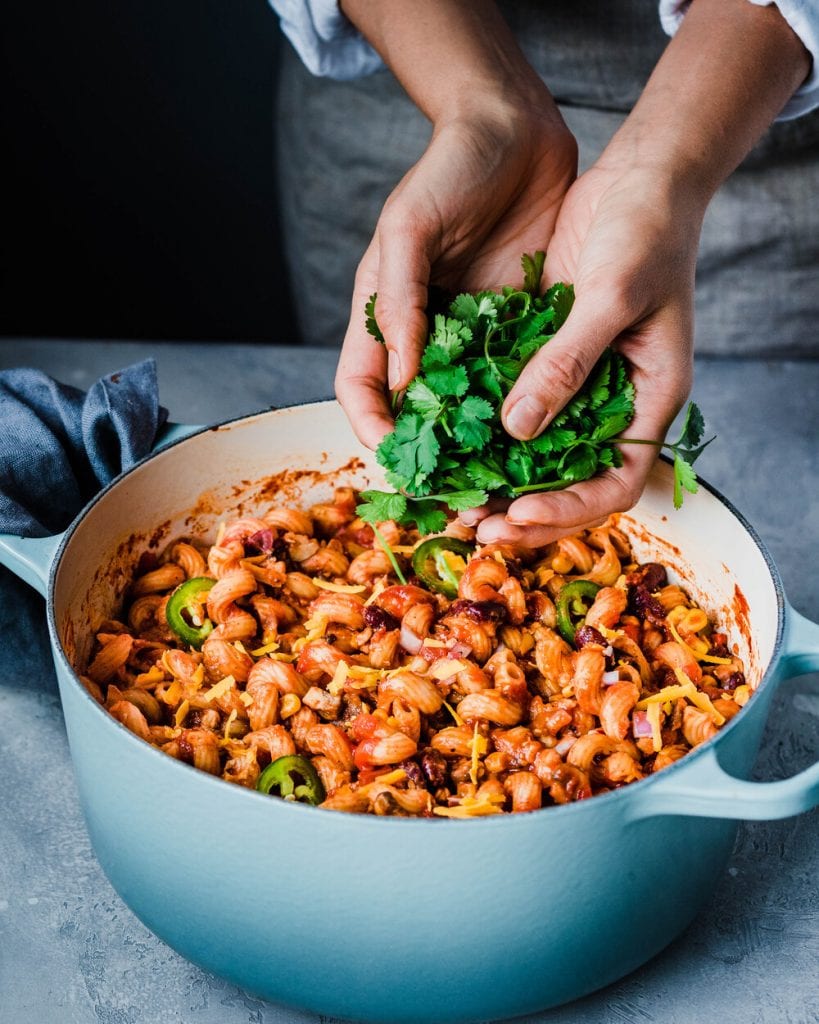 woman's hands adding cilantro to pot of vegan chili mac and cheese