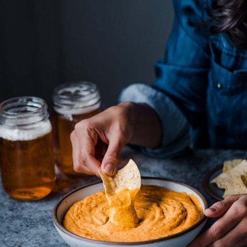 dipping tortilla chip into a bowl of cheesy buffalo cauliflower dip