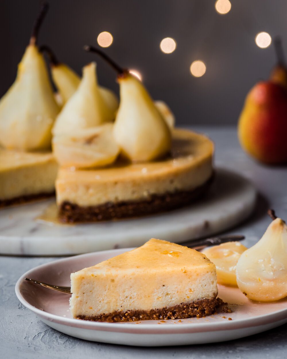 One piece of cheesecake and two poached pear halves on a plate with a fork.