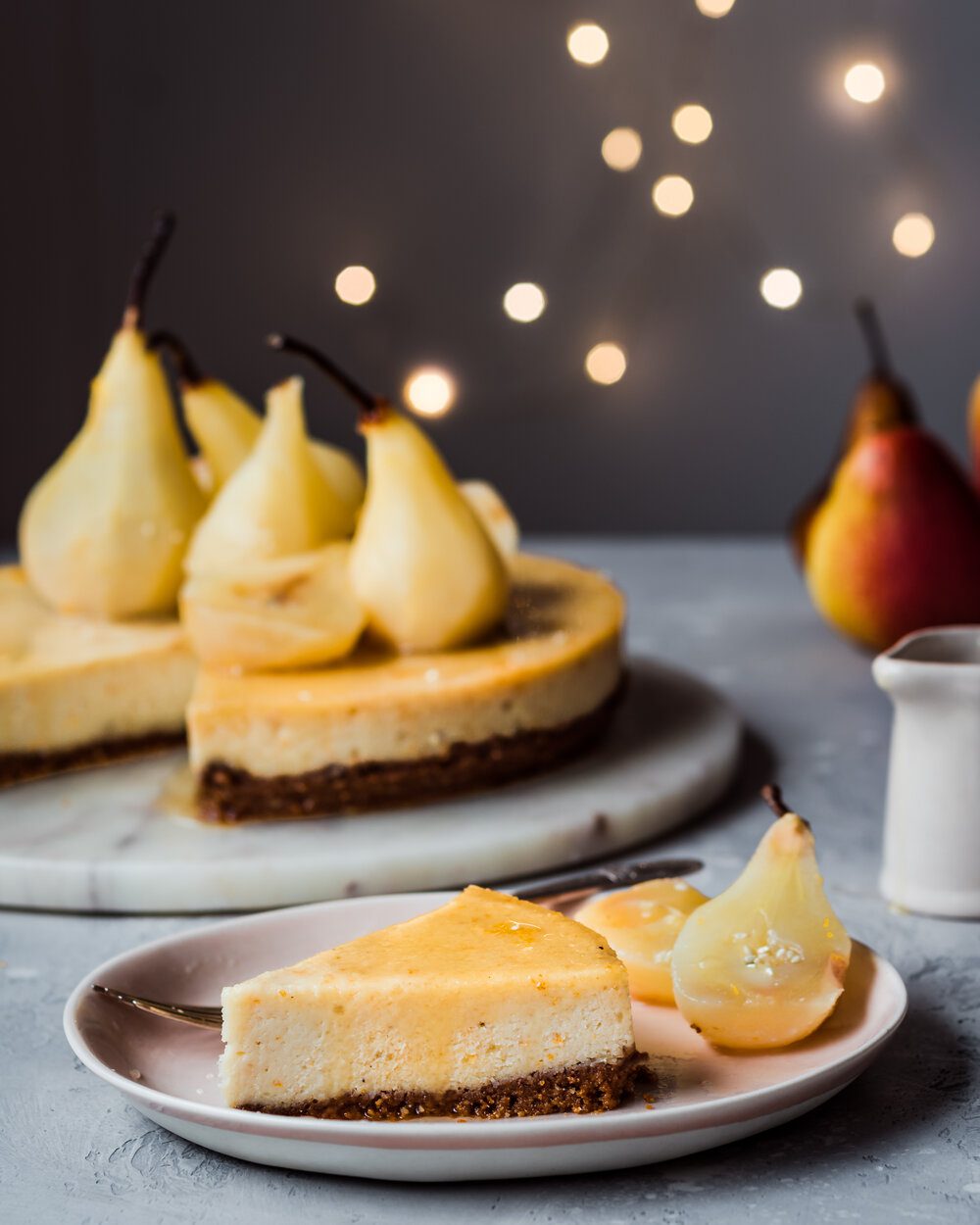 Piece of cheesecake and two poached pear halves on a plate with a fork.