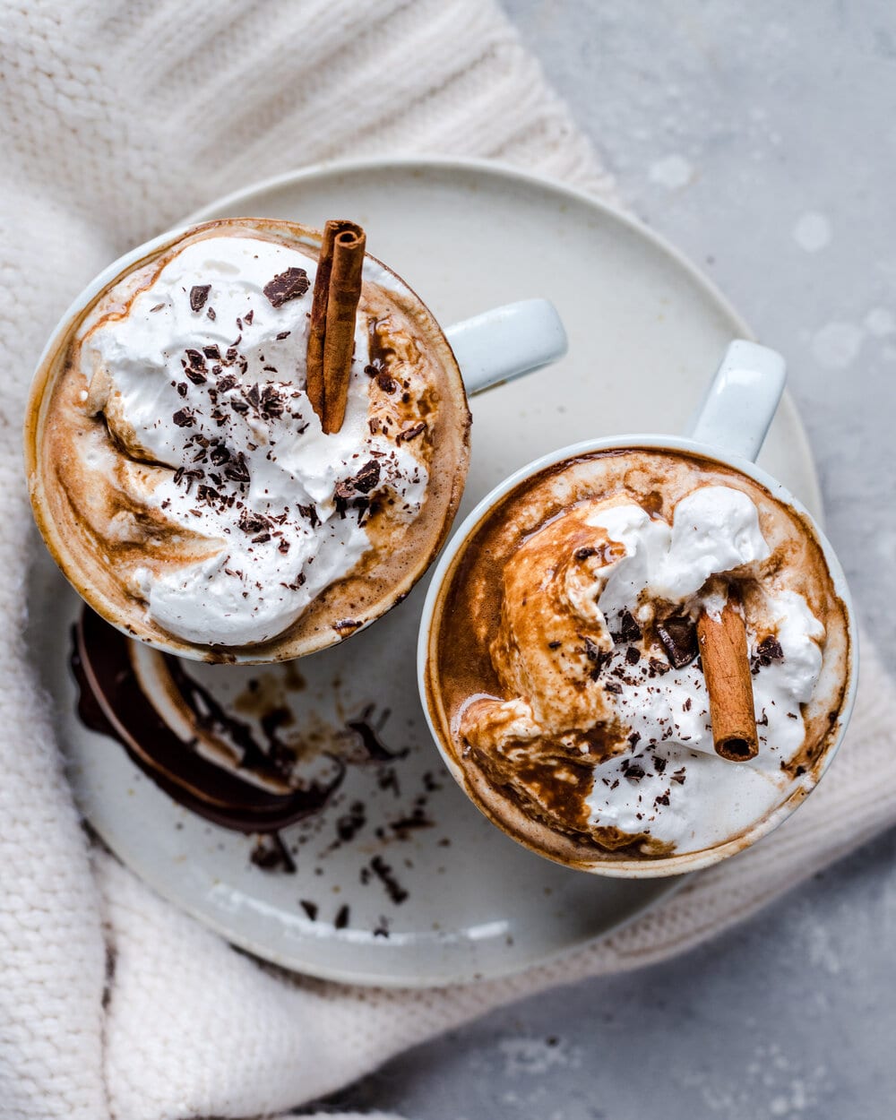 Overhead view of hot chocolate in two white mugs on a white plate.