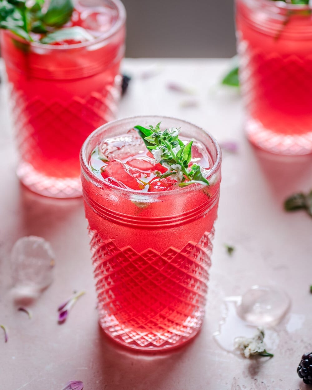 Three glasses of blackberry lemonade on a pink table.