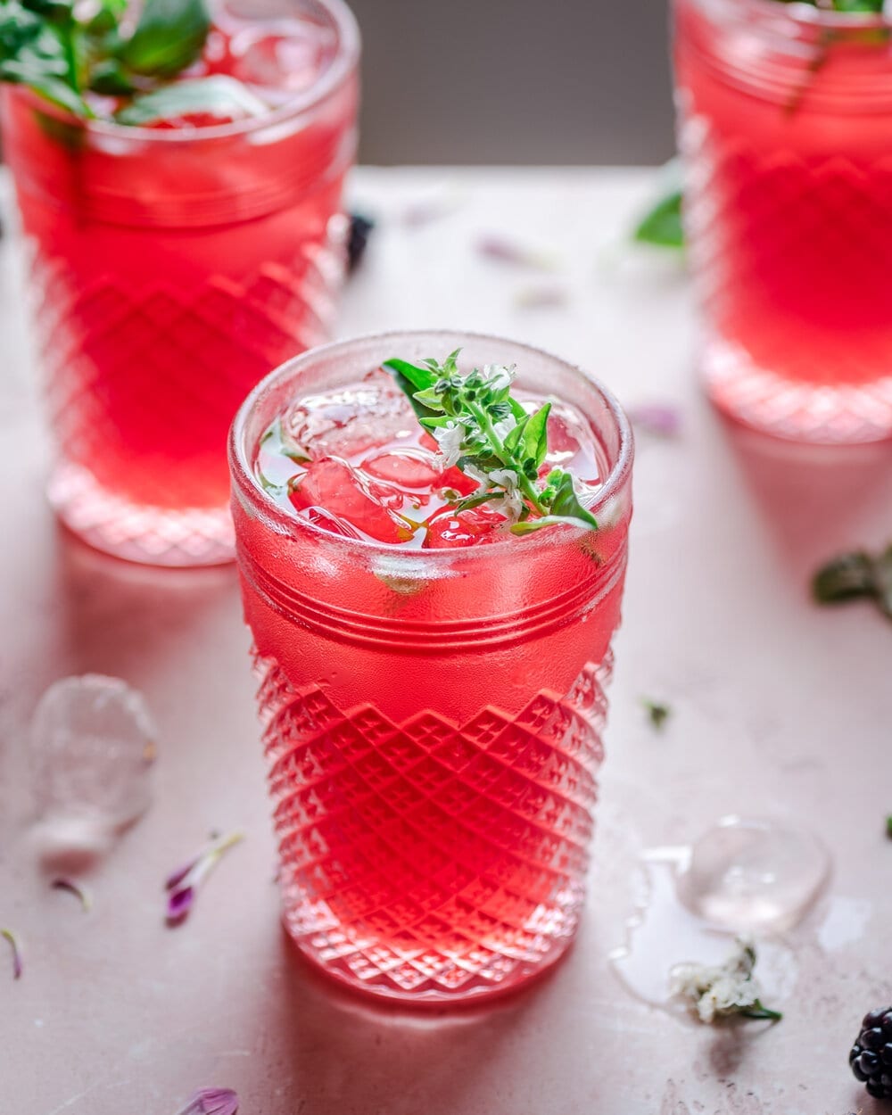 cups full of blackberry lemonade on a pink table.