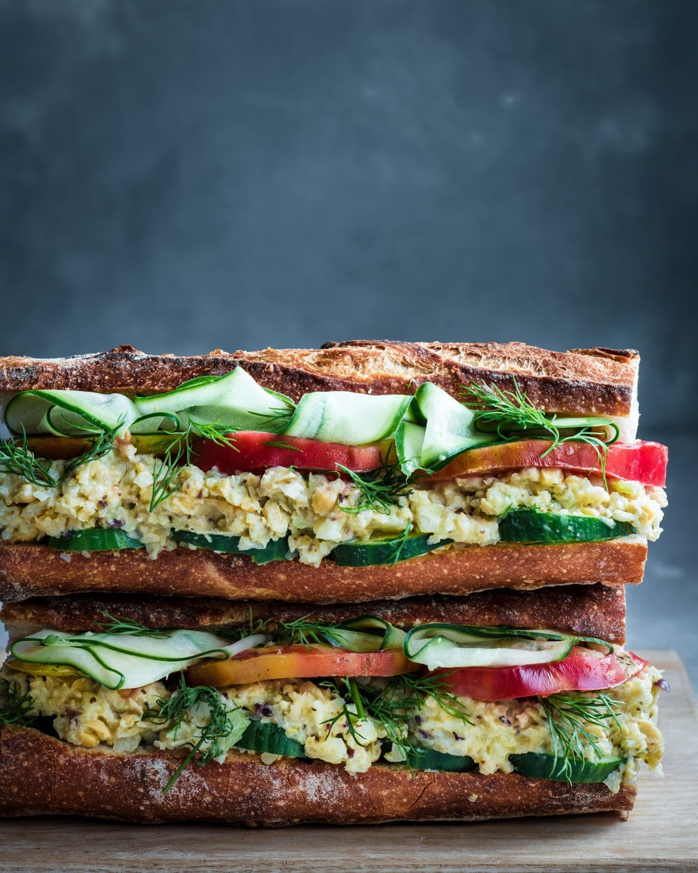 Two Vegan Tuna Salad Sandwiches stacked on a wooden cutting board.