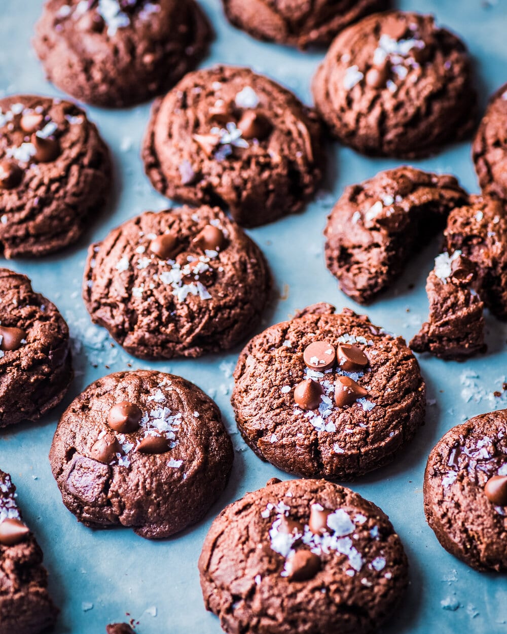 Vegan Triple Chocolate Cookies sprinkled with flaky salt on a grey table.