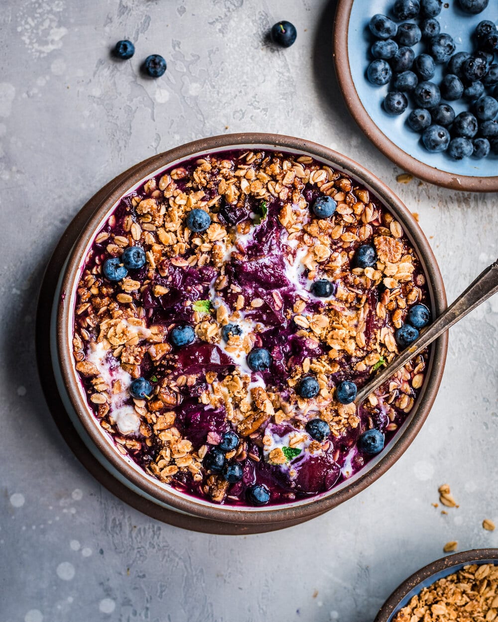 Berry Crisp in a bowl with a spoon on a grey table.