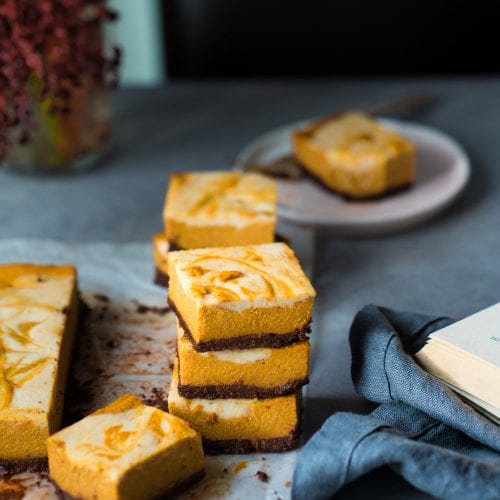 Three cheesecake bars stacked in a pile. Next to other cheesecake bars.