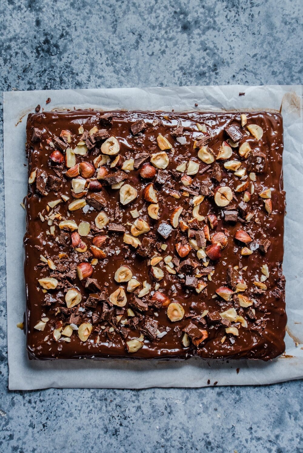 Full unsliced square brownie square with toppings on a piece of parchment paper.