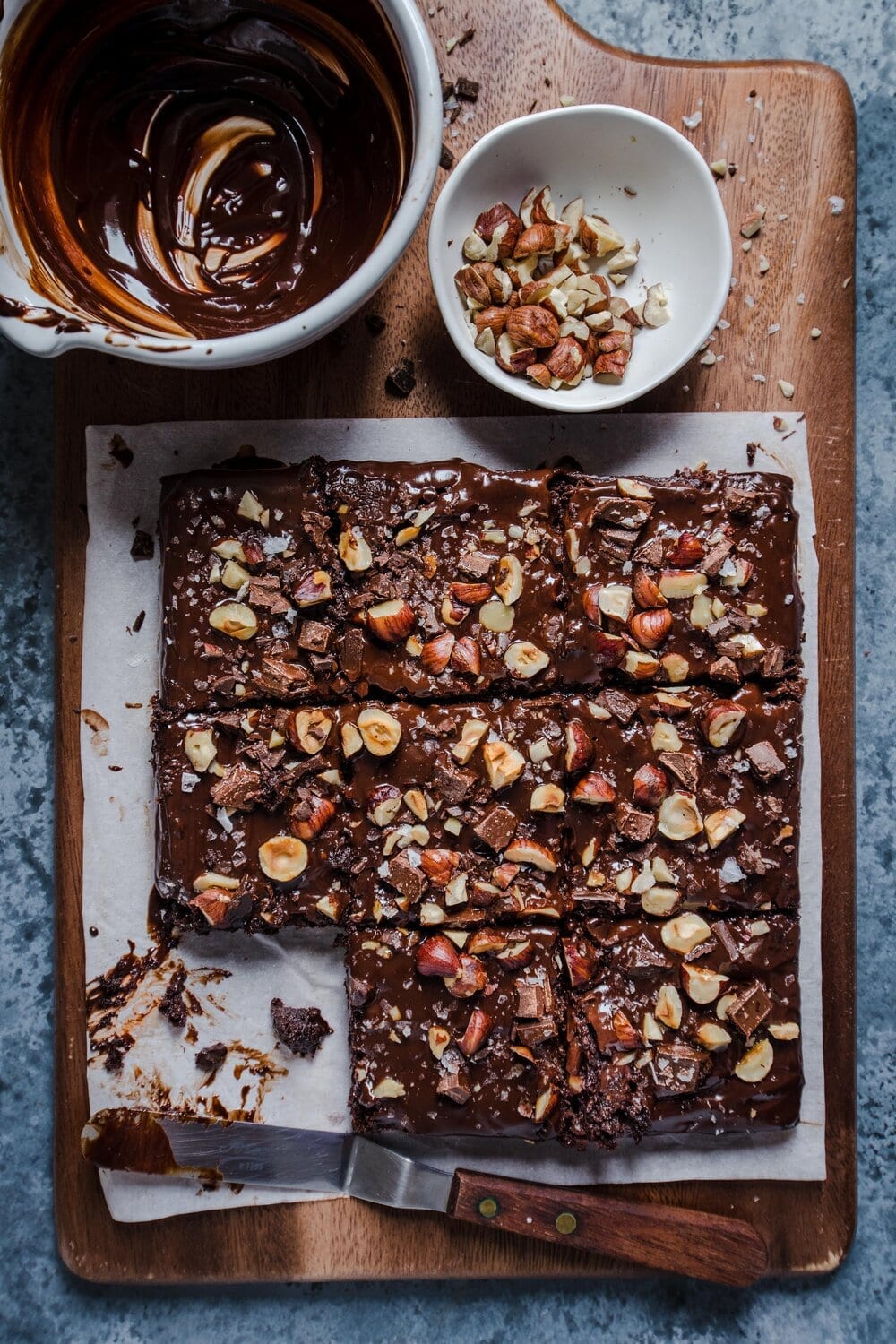 Brownie square with toppings on a piece of parchment paper on a wood cutting board.