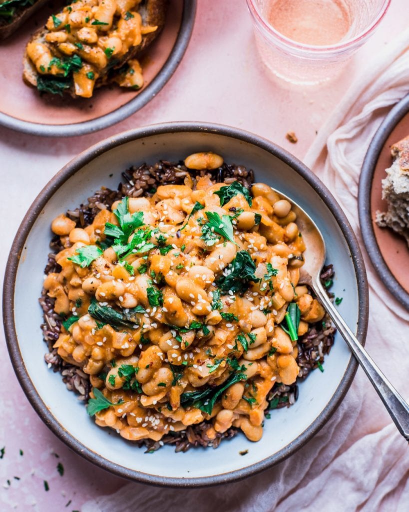 ceramic bowl on pink backdrop with creamy white beans and kale served over wild rice