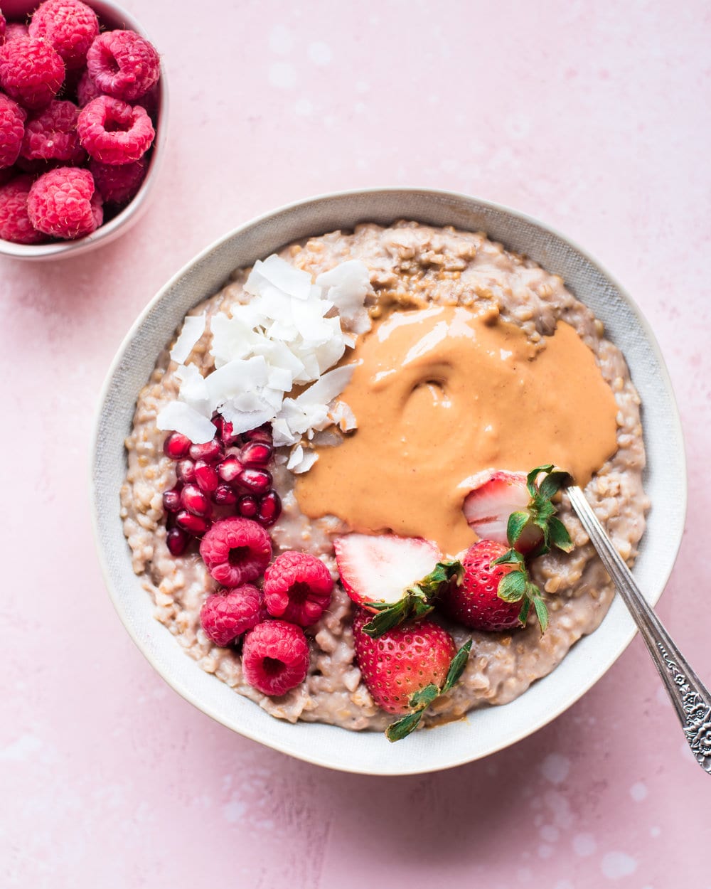 Oatmeal with peanut butter and strawberries in a white bowl on a pink table.