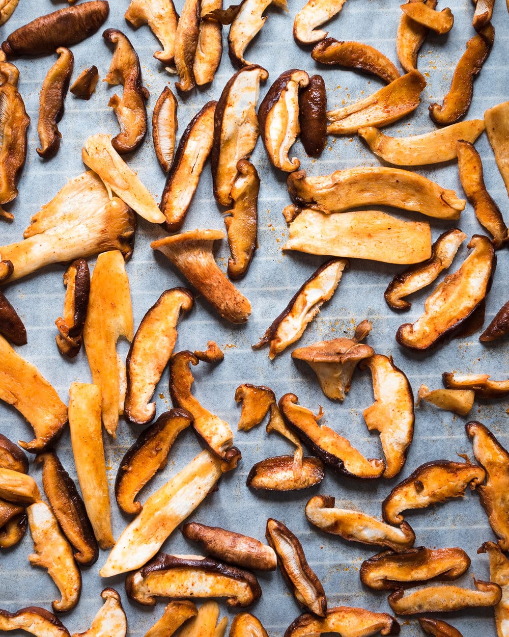 Thinly sliced marinated mushrooms on a piece of parchment paper on baking tray.