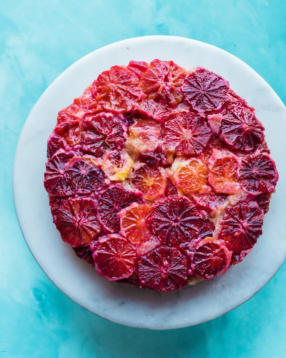 Full blood orange cake on a white marble serving board.