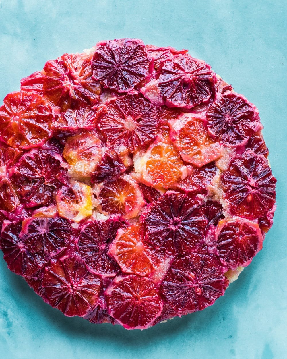 Full blood orange cake on a blue table.