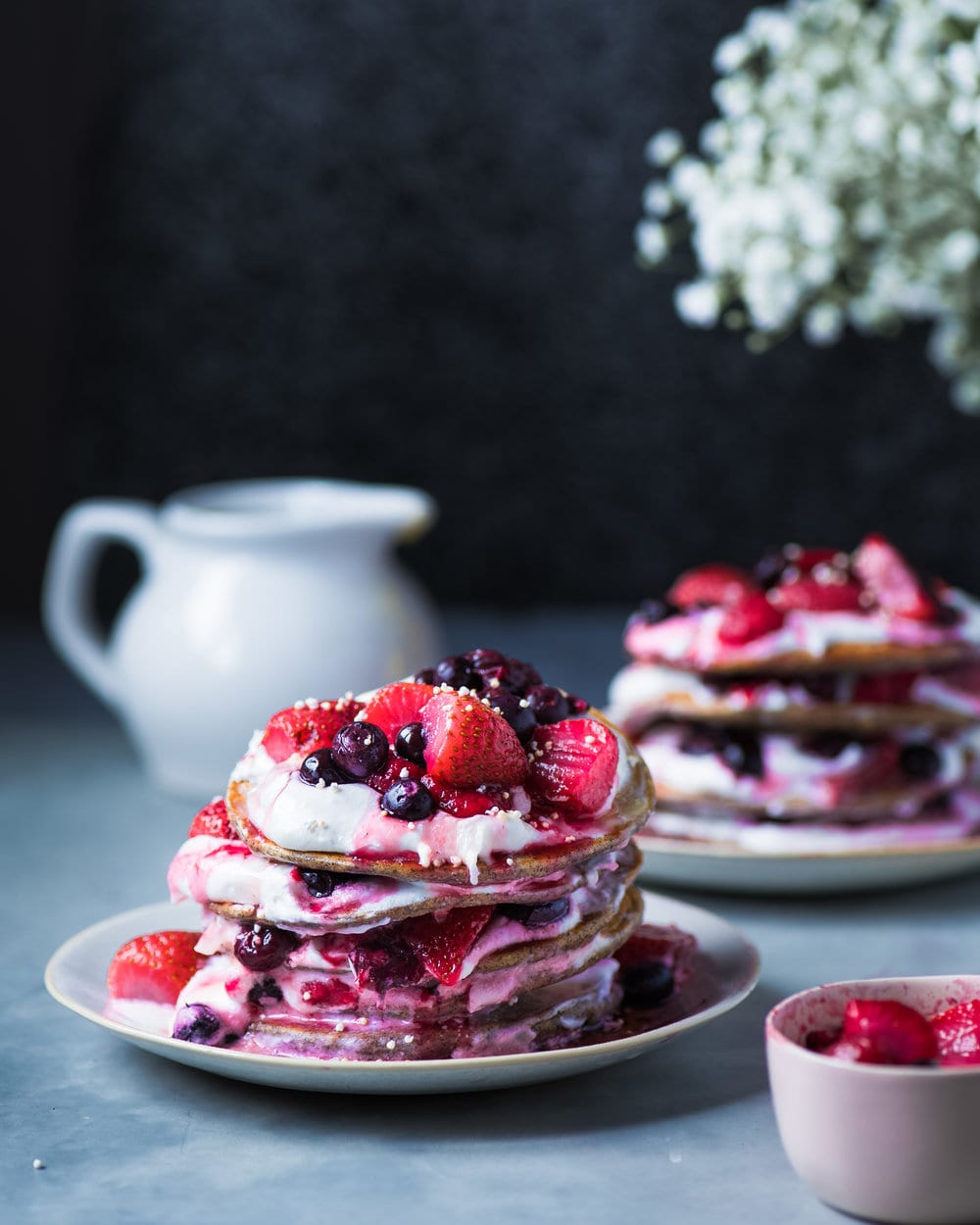 Two grey plates stacked high with pancakes layered with vegan yogurt and berries.