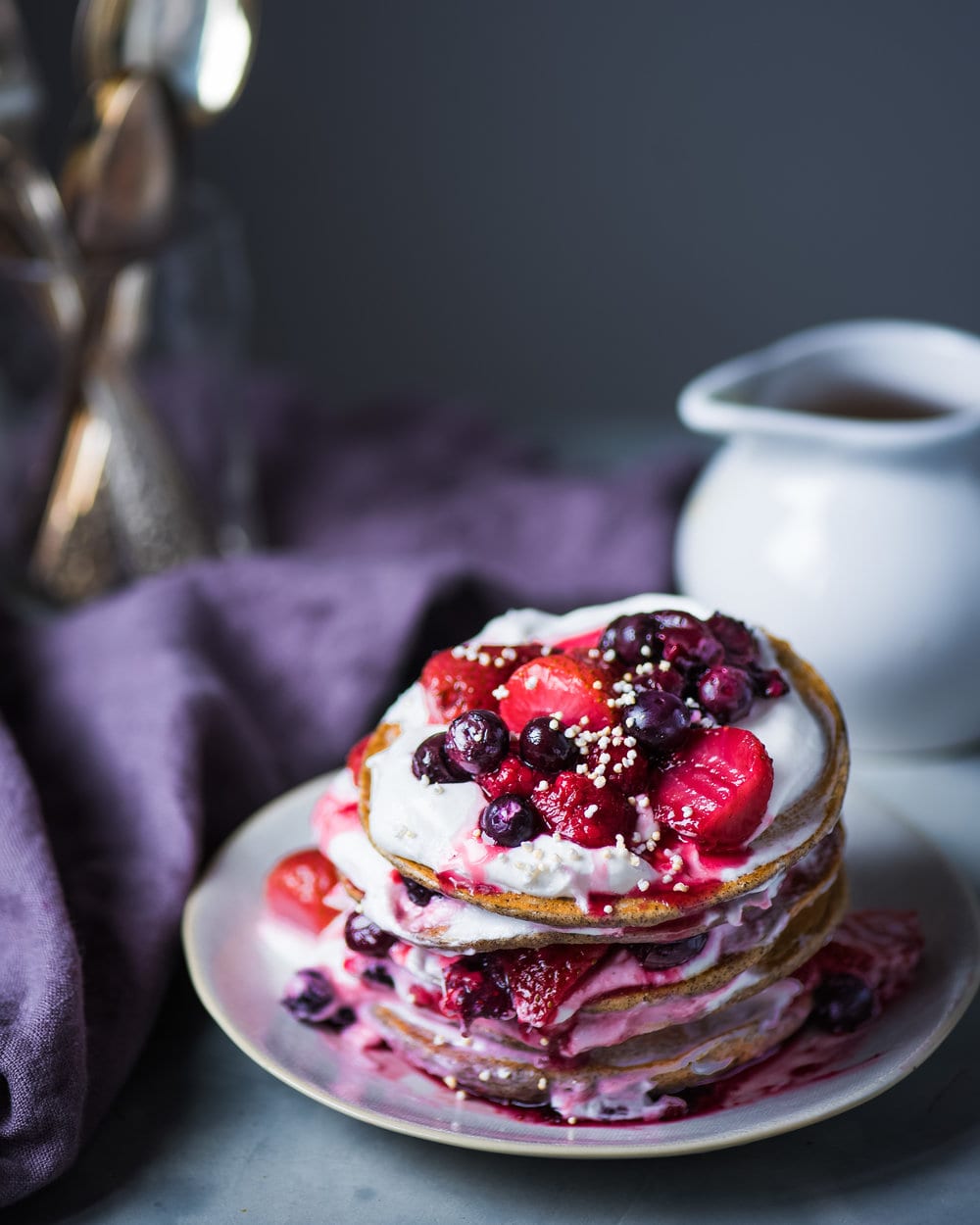 Grey plate stacked high with pancakes layered with vegan yogurt and berries.