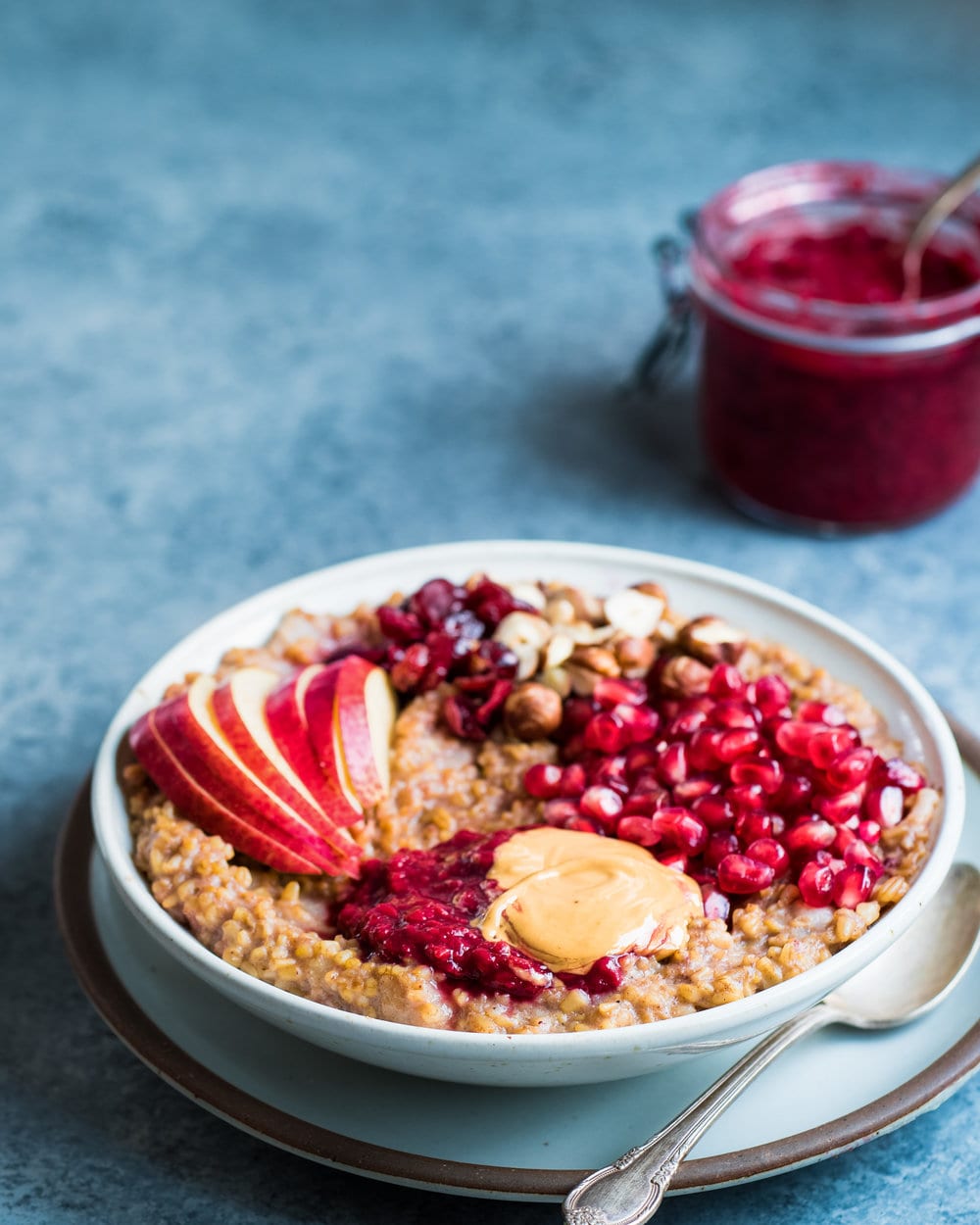 Large white bowl filled with oatmeal with toppings and a spoon on a grey counter.